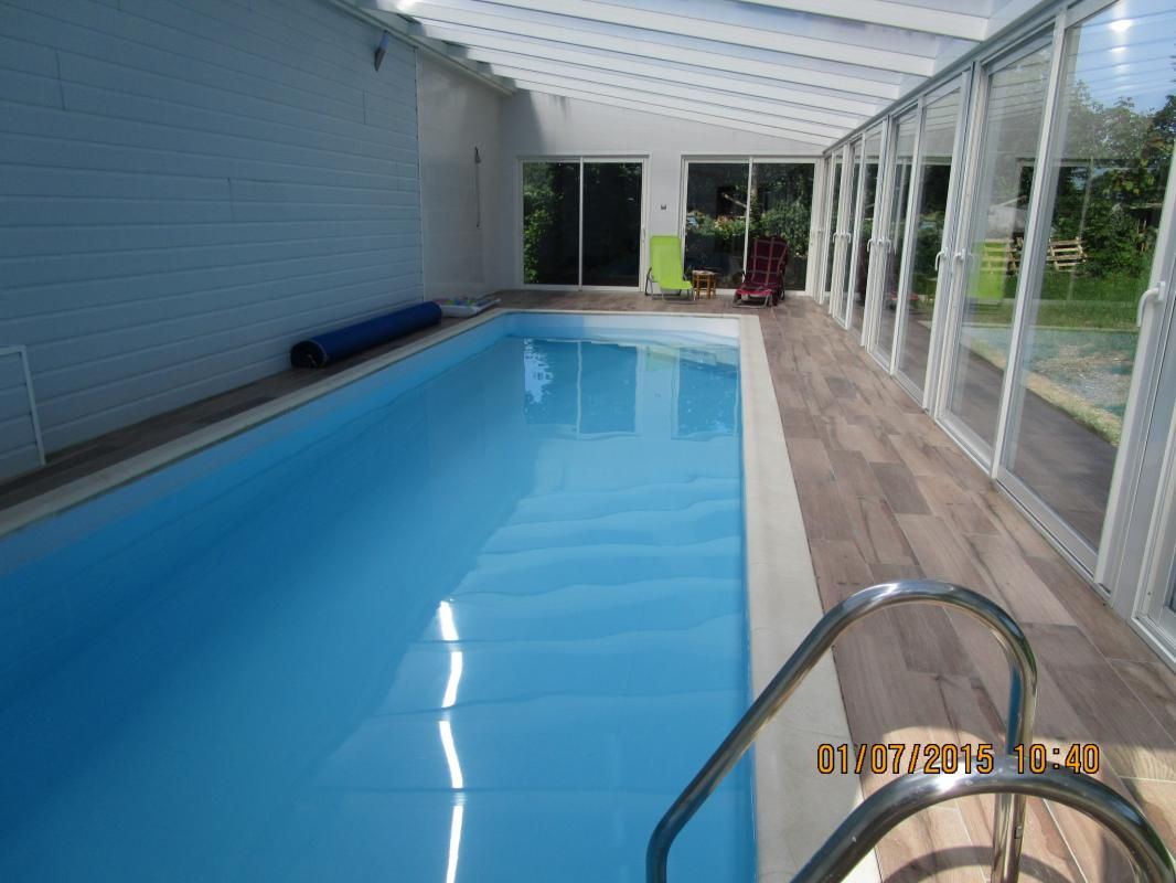 La piscine intérieure chauffée, sous une véranda vitrée donnant sur le jardin
